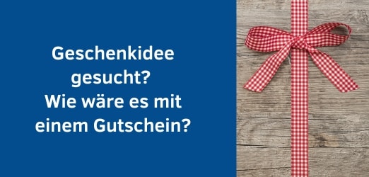 Es ist auf einem Holhintergrund eine rot-weiß-karierte Geschenkschleife zu sehen. Text: Geschenkidee gesucht? Wie wäre es mit  einem Gutschein?
